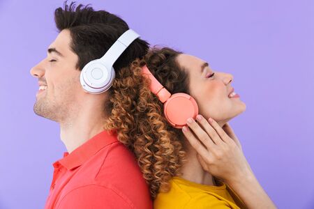 Portrait of beautiful couple smiling and listening to music with headphones standing back to back...