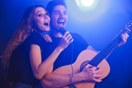 Image of young positive optimistic loving couple musicians group duet on scene in night club over dark background with flash lights.の写真素材