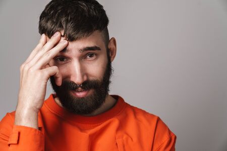 Image closeup of young bearded man with nose jewelry wearing orange shirt smiling at camera isolated over gray backgroundの写真素材