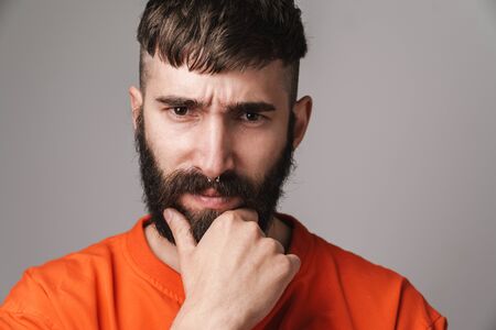 Image closeup of young bearded man with nose jewelry wearing orange shirt looking at camera isolated over gray backgroundの写真素材