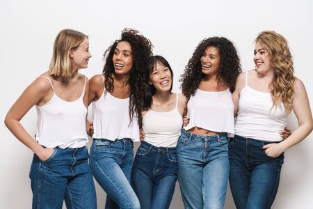 Image of joyful multinational women in blue jeans smiling and hugging together isolated over whiteの写真素材