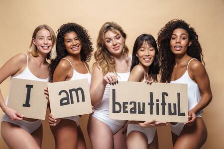 Image of young multinational women in underclothes smiling and holding placards isolated over beigeの写真素材