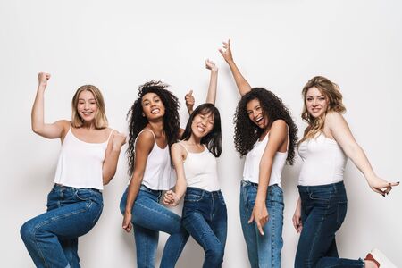 Image of excited multinational women in blue jeans smiling and making winner gesture isolated over whiteの写真素材