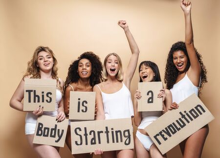 Image of excited multinational women in underclothes screaming and holding placards isolated over beigeの写真素材
