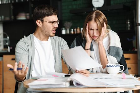 Image of confused young businesslike man and woman doing calculations and paperwork together in cafe
