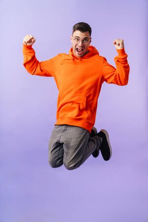 A happy emotional young man jumping wearing eyeglasses showing winner gesture.