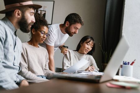 Multiethnic young female and male colleagues discussing business ideas at table while working in officeの写真素材