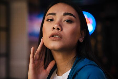 Photo of seductive young asian woman with brunette hair looking at camera while posing in cafeの写真素材