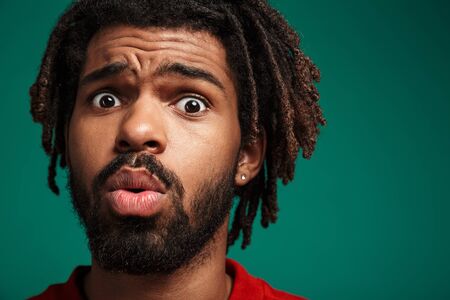 Close up portrait of a shocked young african man wearing pullover standing isolated over green...