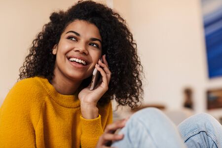 Image of smiling african american woman talking on cellphone while sitting on floor in living roomの写真素材