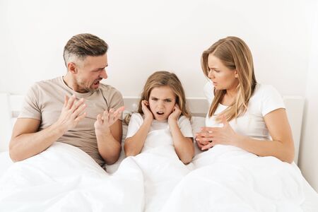 Photo of displeased caucasian parents scolding their stressed daughter while sitting in white badの写真素材