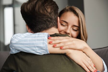 Photo closeup of happy romantic caucasian couple smiling and hugging while sitting on sofa at home