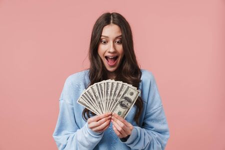 Image of attractive young woman with long brown hair rejoicing and holding dollar banknotes isolated...