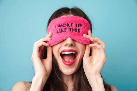 Photo closeup of excited young woman holding posing in sleeping mask isolated over blue wallの写真素材