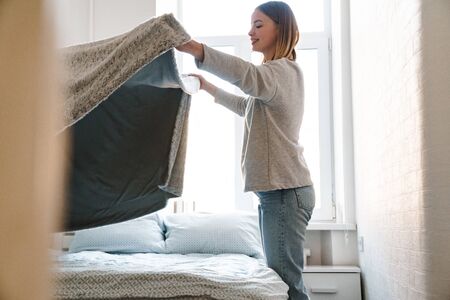 Smiling attractive blonde girl making bed in the morning