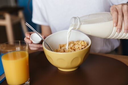 Close up of a young woman having a healthy breakfast while sitting at the kitchen table, pouring...