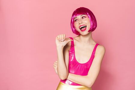 Image of joyful party girl wearing wig laughing and pointing thumb at herself isolated over pink backgroundの写真素材