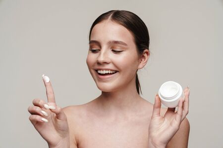 Image of pleased young shirtless woman showing face cream and smiling isolated over grey backgroundの写真素材