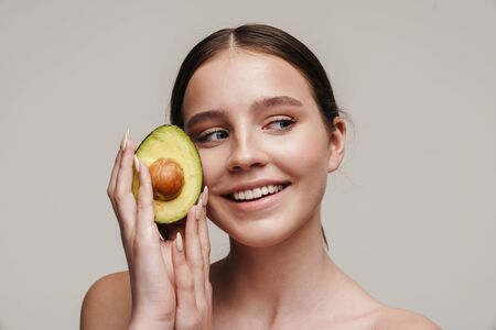 Image of joyful nice shirtless woman smiling while posing with avocado isolated over grey backgroundの写真素材
