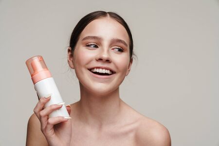 Image of pleased young shirtless woman holding face foam and smiling isolated over grey backgroundの写真素材