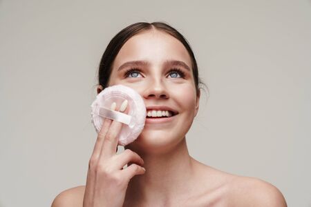 Image of pleased young shirtless woman using makeup pad and smiling isolated over grey backgroundの写真素材