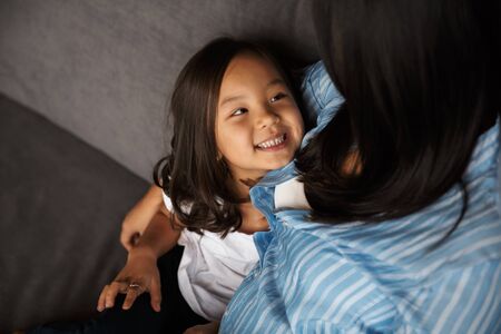 Photo of young pregnant asian woman with her little daughter hugging and smiling while sitting on...