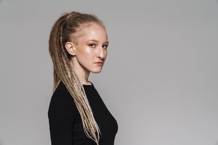 Portrait of an attractive confident young woman with dreadlocks standing isolated over gray...