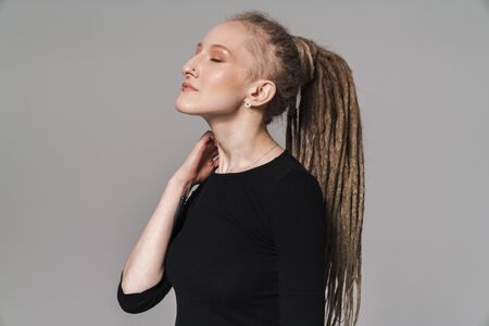 Portrait of an attractive smiling young woman with dreadlocks standing isolated over gray...