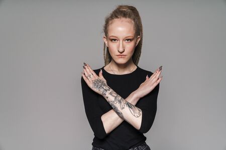 Portrait of an attractive confident young woman with dreadlocks standing isolated over gray background, showing stop gestureの写真素材