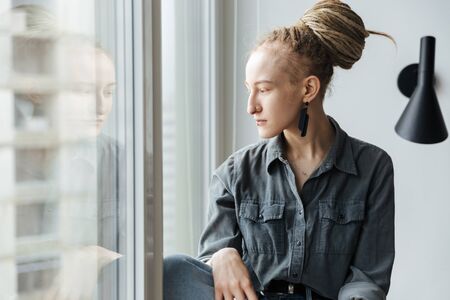 Image of a serious young girl with dreadlocks and piercing indoors near window.の写真素材