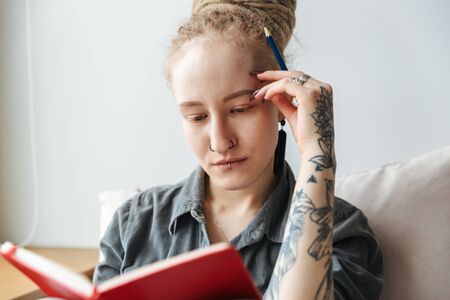 Image of a serious concentrated amazing young girl with dreadlocks writing notes indoors.の写真素材