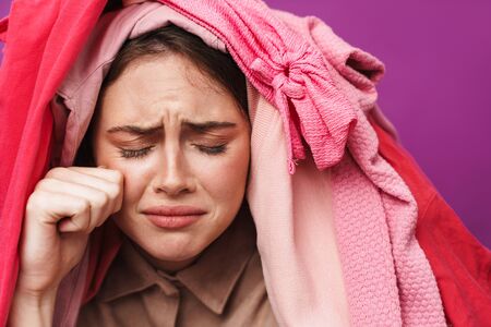 Photo of upset attractive woman with clothes on her head crying on camera isolated over violet wallの写真素材