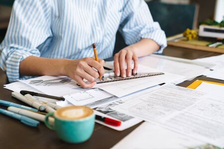 Cropped photo of caucasian woman architect making drawing while designing draft at workplace