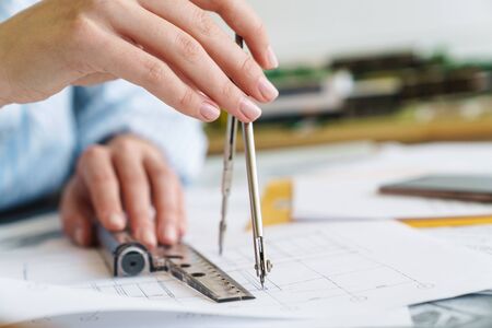 Cropped photo of caucasian woman architect making drawing with compass while designing draft at...
