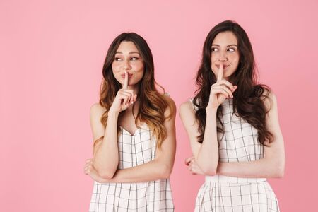 Image of joyful caucasian women smiling and making silence gesture isolated over pink backgroundの写真素材