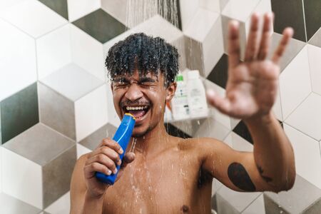 Photo of cheerful half-naked african american man making fun while taking shower in bathroomの写真素材