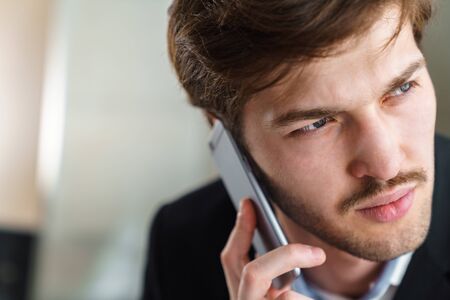 Photo closeup of caucasian brutal businessman with mustache talking on cellphone indoorの写真素材