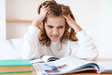 Photo of caucasian displeased girl grabbing her head while doing homework in living room