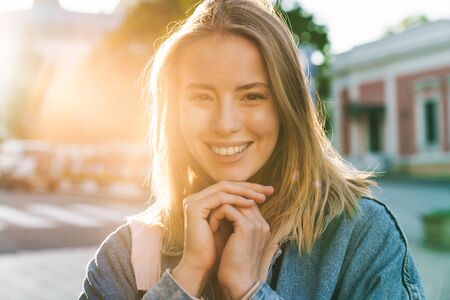Beautiful cheerful young blonde woman wearing denim jacket walking in the city, looking at cameraの写真素材