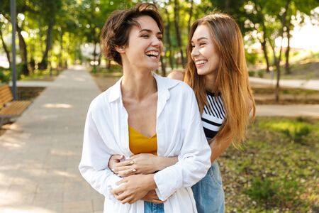 Photo of two beautiful women hugging together and laughing while walking in green parkの写真素材