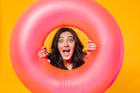 Image of excited caucasian woman posing with rubber ring expressing surprise isolated over yellow wallの写真素材