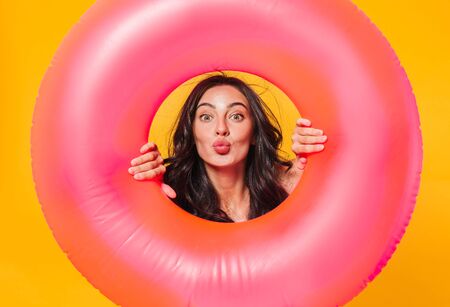 Image of beautiful caucasian woman posing with rubber ring making kiss lips isolated over yellow...