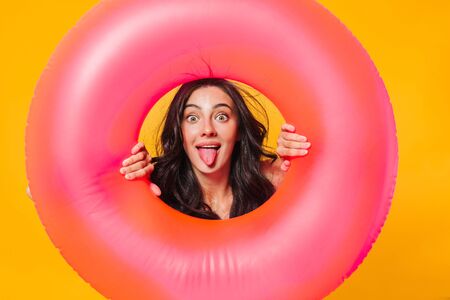Image of amusing caucasian woman posing with rubber ring sticking out her tongue isolated over yellow wallの写真素材