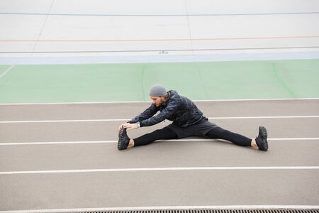 Motivated young fit sportsman working at the stadium racetrack, doing stretching exercises