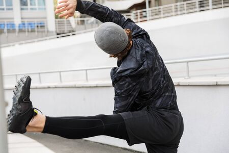 Motivated young fit sportsman working at the stadium racetrack, doing stretching exercises
