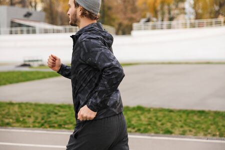 Side view of a confident young fit sportsman running on the race track at the stadium outdoors
