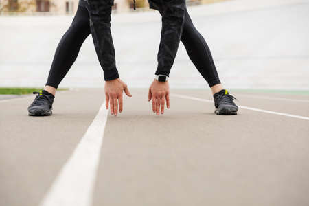 Cropped image of a young fit sportsman working at the stadium racetrack, doing stretching exercises