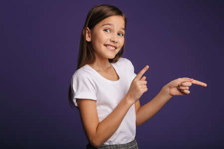 Photo of joyful attractive girl smiling and pointing fingers aside isolated over purple background