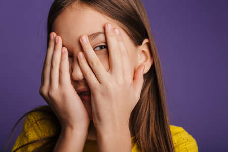 Photo of amusing beautiful girl smiling and covering her face isolated over purple backgroundの写真素材