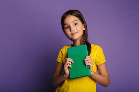 Photo of pleased caucasian girl smiling and holding book isolated over purple background